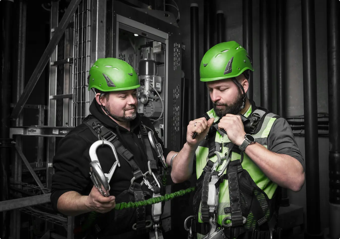 Zwei Mitarbeiter von GRZIB mit grünen Helmen beim Sichern in einem Windkraft-Aufzug.